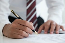 Close up businessman signing legle agreement document contract with partnership agreement after successful negotiation deal.